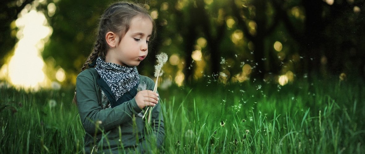 Mädchen mit einer Pusteblume auf einer Wiese